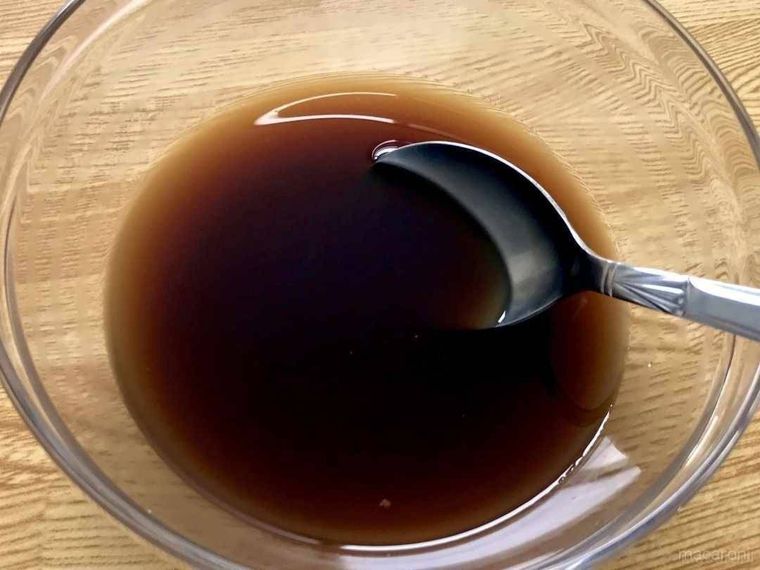 透明なボウルに入った生姜焼きのタレに、銀スプーンが添えられている様子