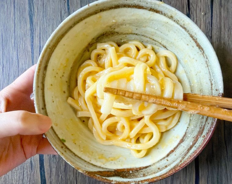 うどんを卵、しょうゆと混ぜる様子