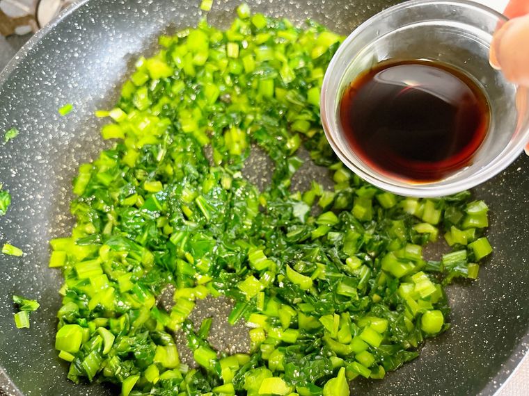 炒めた小松菜にしょうゆを入れる様子