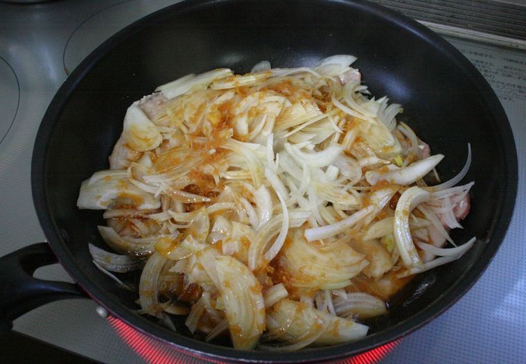 フライパンで焼いた豚ロース肉の上に玉ねぎをのせ、たれを入れた様子
