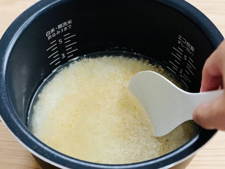 炊飯釜に米、水、コンソメを入れ、かき混ぜている様子