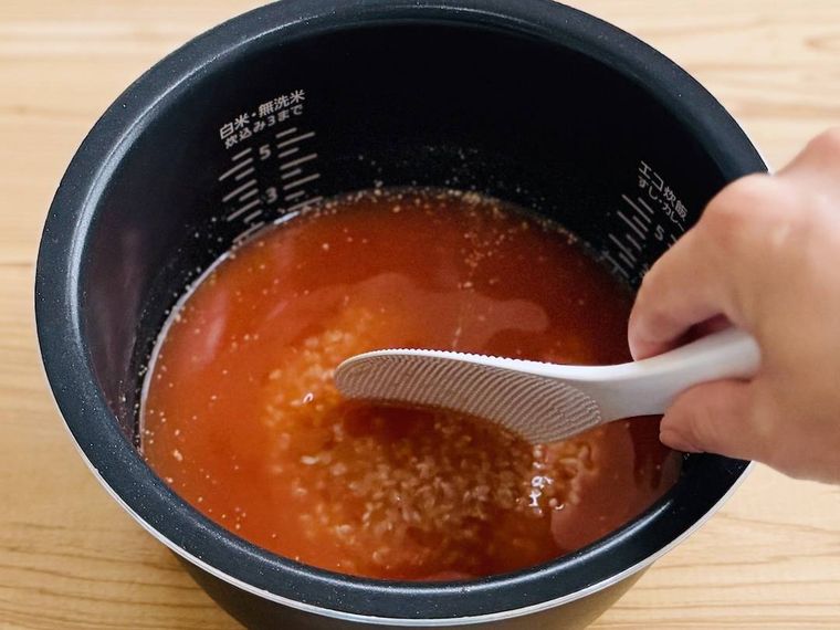 炊飯釜に、米、ケチャップ、コンソメ、水を入れ、かき混ぜている様子