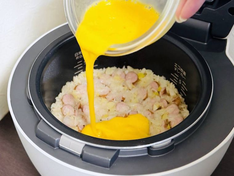 チャーハンが入った炊飯釜に溶き卵を回し入れている様子
