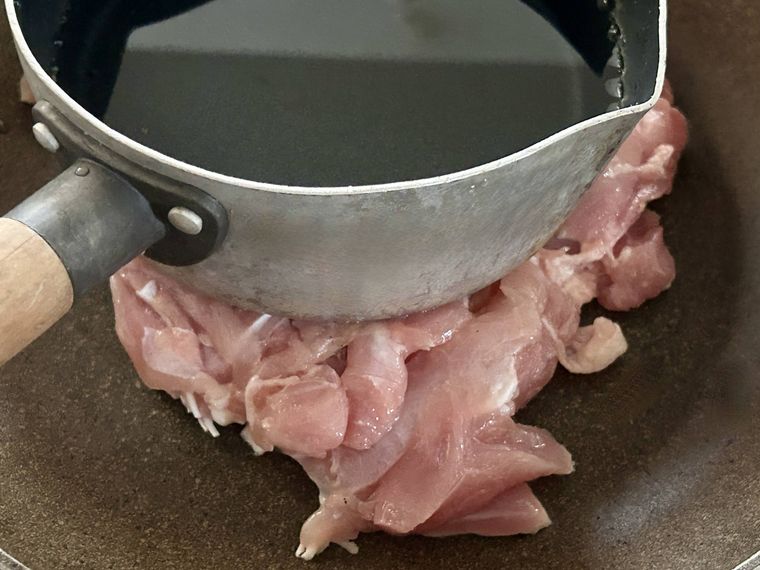 鶏もも肉の上に水の入った鍋が置かれているところ