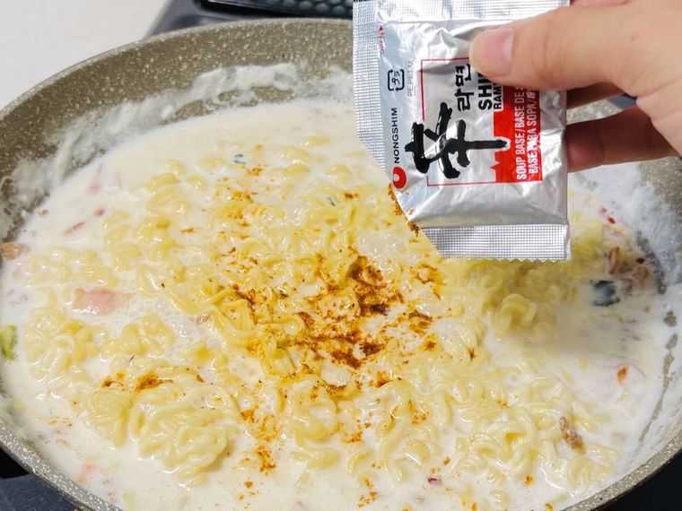 牛乳と水で煮た辛ラーメンに粉末スープを加えている様子