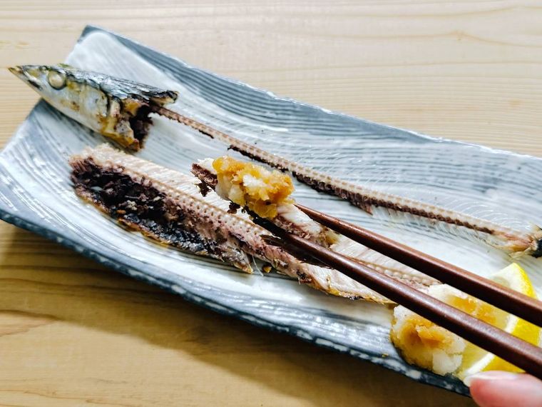 焼きさんまに大根おろしをのせて箸でつかんだ様子