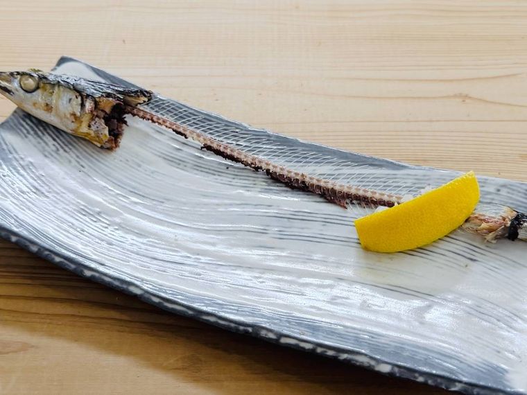食べ終わった焼きさんまの頭、中骨、レモンを皿の箸に寄せた様子