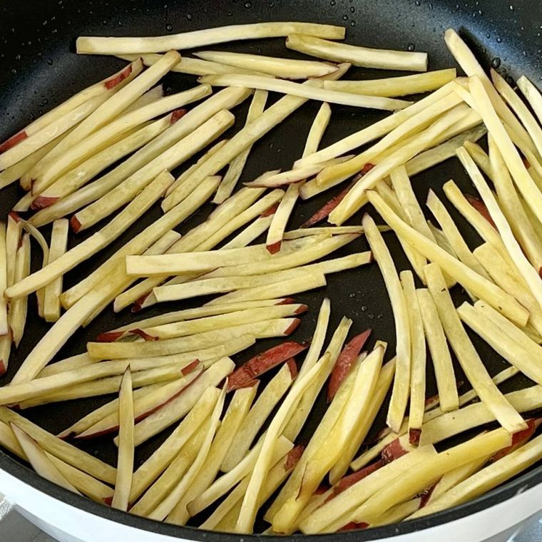 フライパンに並んだ炒める前の棒状のさつまいも