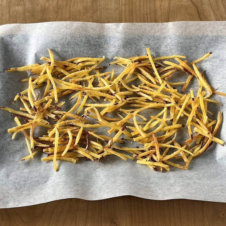 クッキングペーパーをしいた天板に並べられたカリカリの芋けんぴ