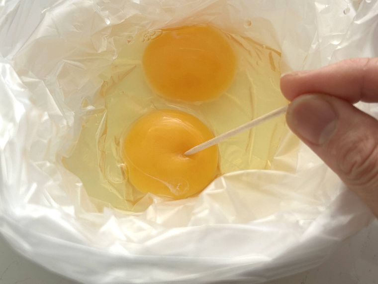 アイラップの中の卵の黄身に爪楊枝で穴を開けているところ