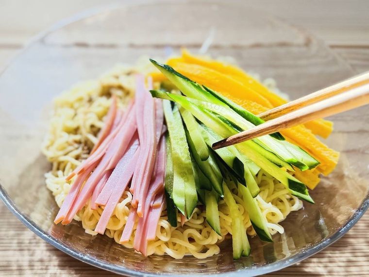 冷やし麺に、ハム、きゅうり、錦糸卵をトッピングしている様子