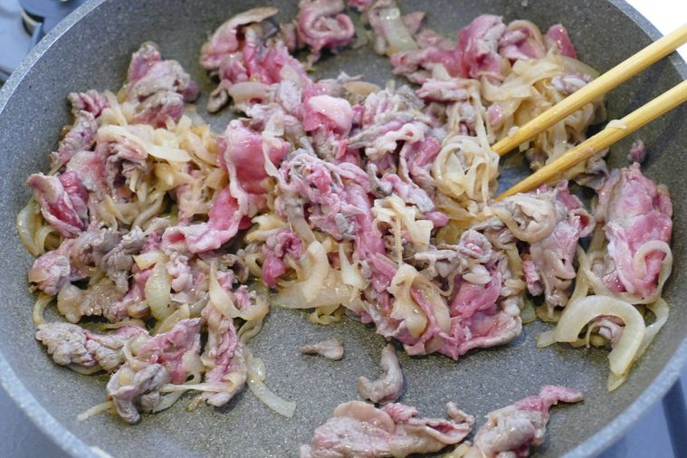 牛こま肉と玉ねぎを箸で混ぜながら炒める様子