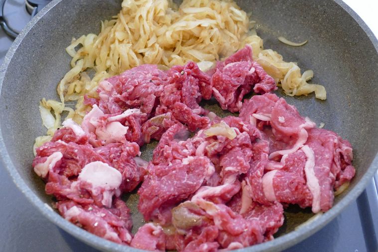 炒め玉ねぎが入っているフライパンに牛こま肉を加えた様子