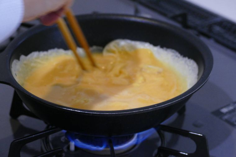 フライパンに卵液を流し入れて菜箸で混ぜながら半熟にする様子