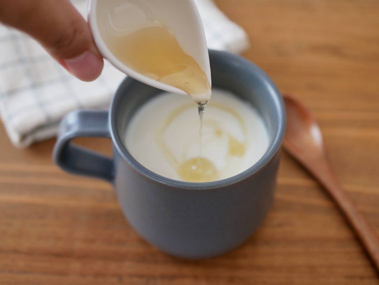 ダークグレーのマグカップに入ったホットヨーグルトにはちみつをかける様子